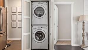 Une buanderie équipée d’un lave-linge et d’un sèche-linge à chargement frontal, dotée d’un plancher en bois et d’une porte donnant sur une autre pièce.