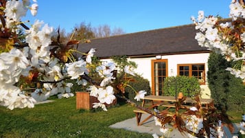 A white building with a dark roof, surrounded by a well-maintained lawn and flowering trees.