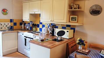 A kitchen with a wooden countertop, a stove, a microwave, and a dining area with a checkered tablecloth.