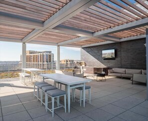 Eine Außenpatio mit einer Holz-Pergola, einer Sitzecke und einem an einer Backsteinmauer befestigten Fernseher.