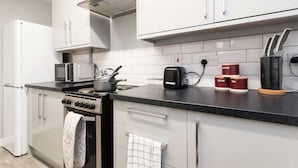 A modern kitchen with white cabinets, a stove, microwave, and a coffee maker. - Coventry- Jenner Pet Friendly 2 Bedroom Apartment (Coventry)