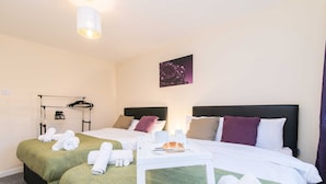 A hotel room with two beds, a bedside table with a tray, towels, and a painting on the wall. - Coventry- Jenner Pet Friendly 2 Bedroom Apartment (Coventry)
