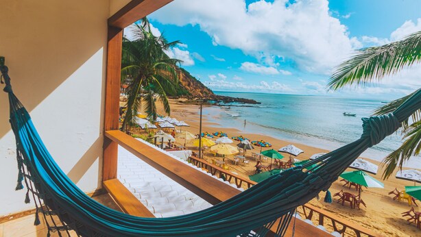 Vista de una hamaca con vista a una playa, con sombrillas y sillas.