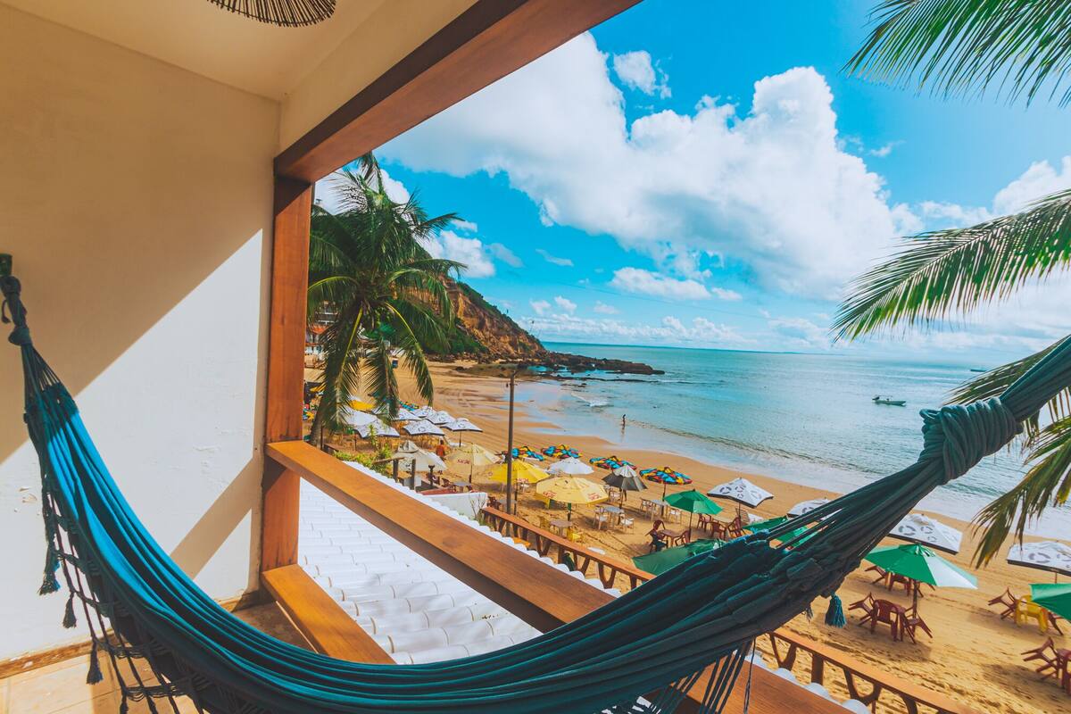 Vista de uma rede com vista para uma praia, com guarda-sóis e cadeiras.