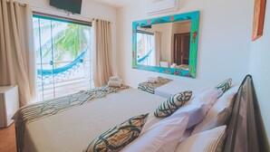 Habitación de hotel con cama, dos ventanas con cortinas, televisor montado, equipo de aire acondicionado y un espejo colorido.