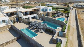 A modern resort with a large swimming pool, outdoor seating areas, and a view of the surrounding landscape.