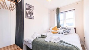 A hotel room with a bed, a window with curtains, a framed picture on the wall, and a wooden bench. - Sublime Stays Parliament 2-bed Apartment (Derby)