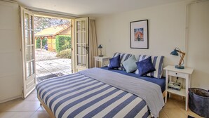 Camera da letto con un letto, un comodino, una lampada, un quadro appeso al muro e una porta aperta su un patio.
