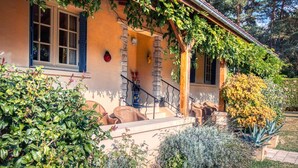 Una casa con una scala in pietra che conduce a un portico, circondata da diverse piante e arbusti.