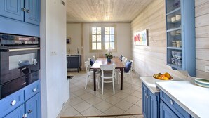 Una cucina con soffitto in legno, un tavolo da pranzo con sedie e pensili contenenti stoviglie.
