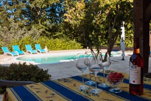 Une table placée au bord de la piscine, avec des verres à vin et une bouteille, entourée de chaises longues bleues et donnant sur la piscine.