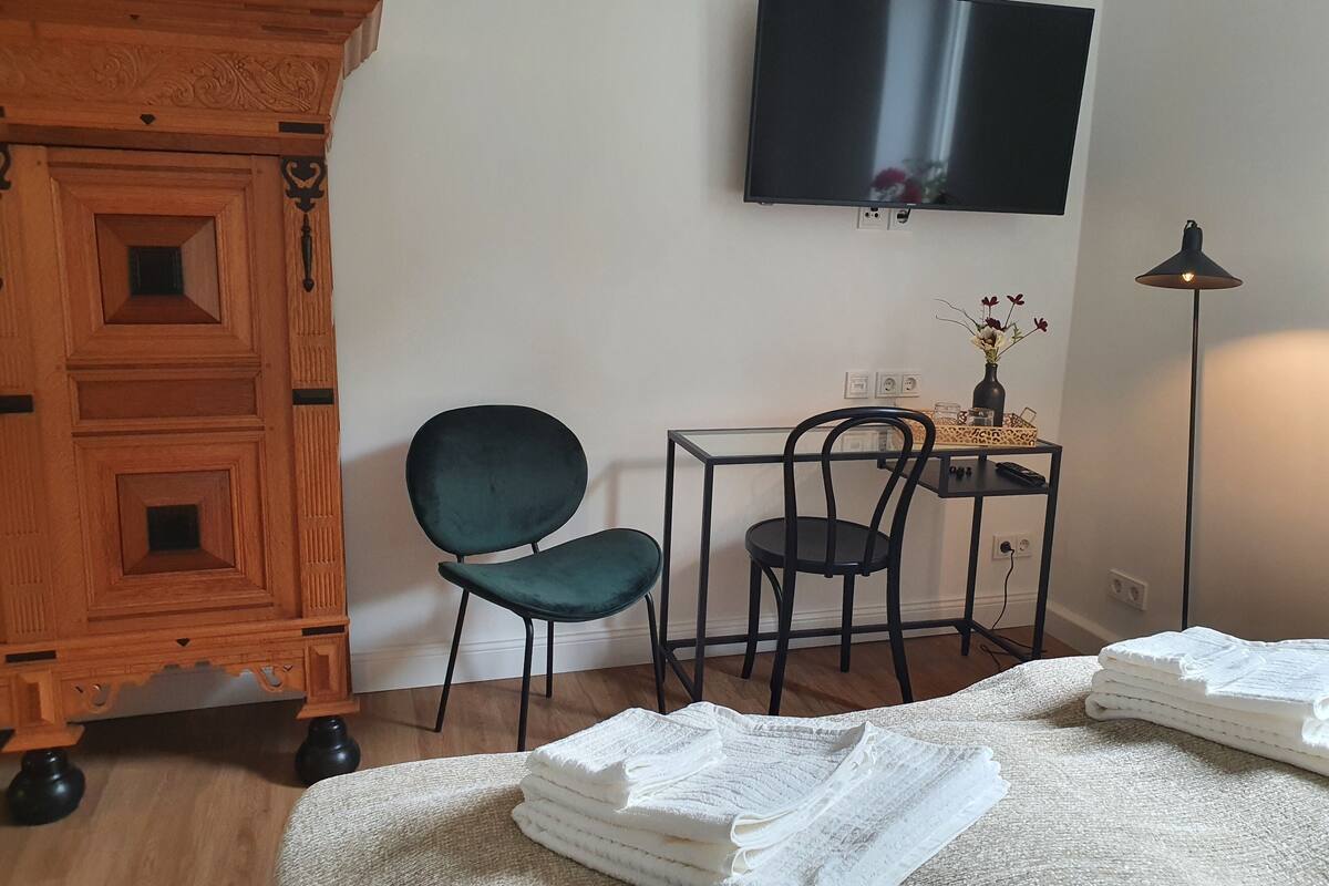 Una habitación con un armario de madera, un escritorio con una silla, un televisor en la pared y una lámpara.
