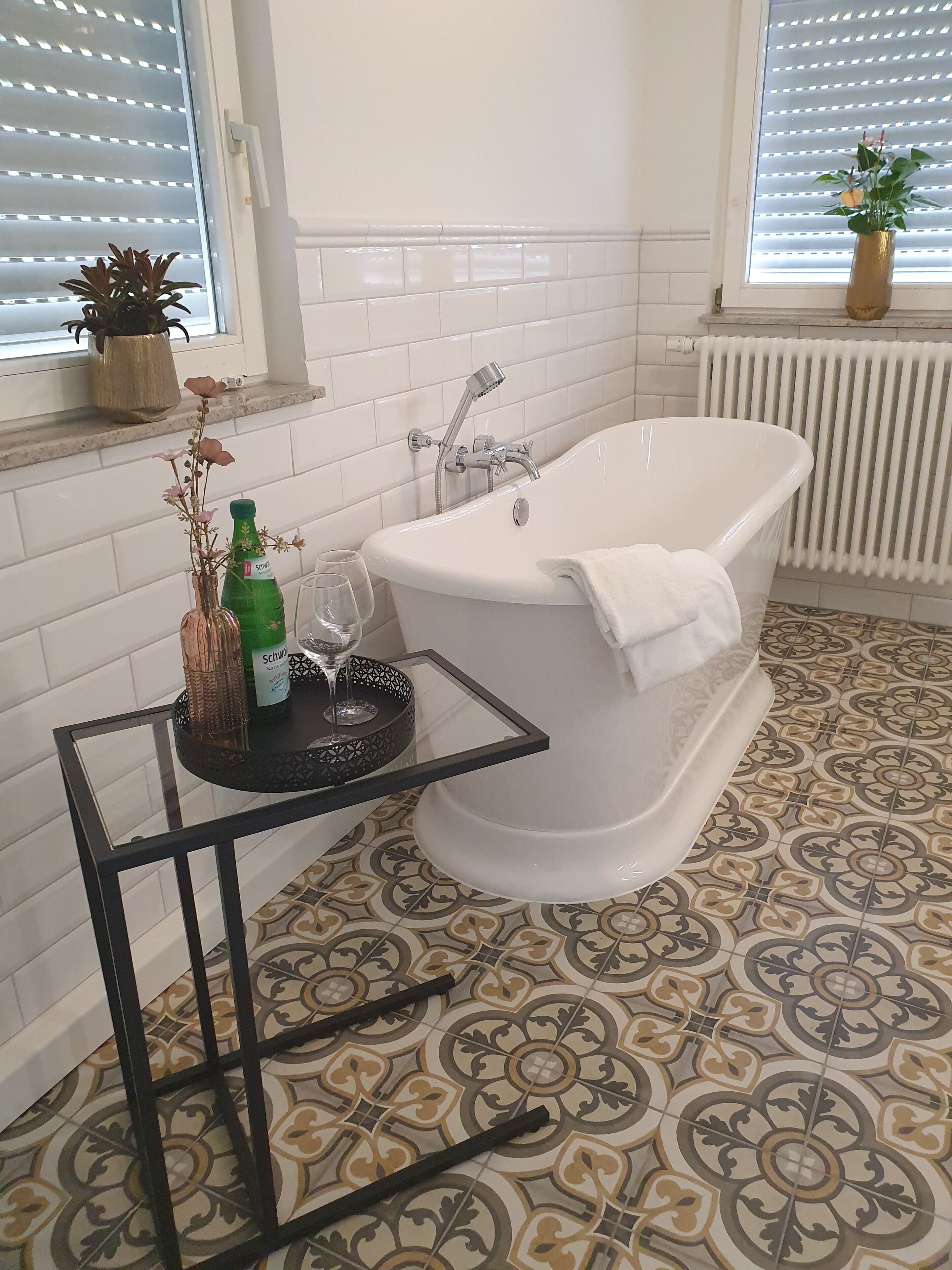 A bathroom with a freestanding bathtub, a potted plant on the windowsill, and a glass of water on a small table.