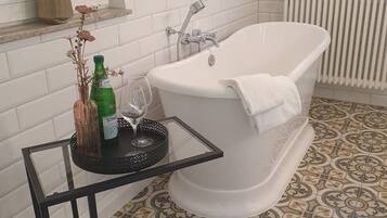 A bathroom with a freestanding bathtub, a potted plant on the windowsill, and a glass of water on a small table.