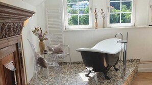 A bathroom with a freestanding bathtub, clear chairs, a wooden cabinet, and patterned tiles. - Boutique Hotel Villa Horbach (Idar-Oberstein)