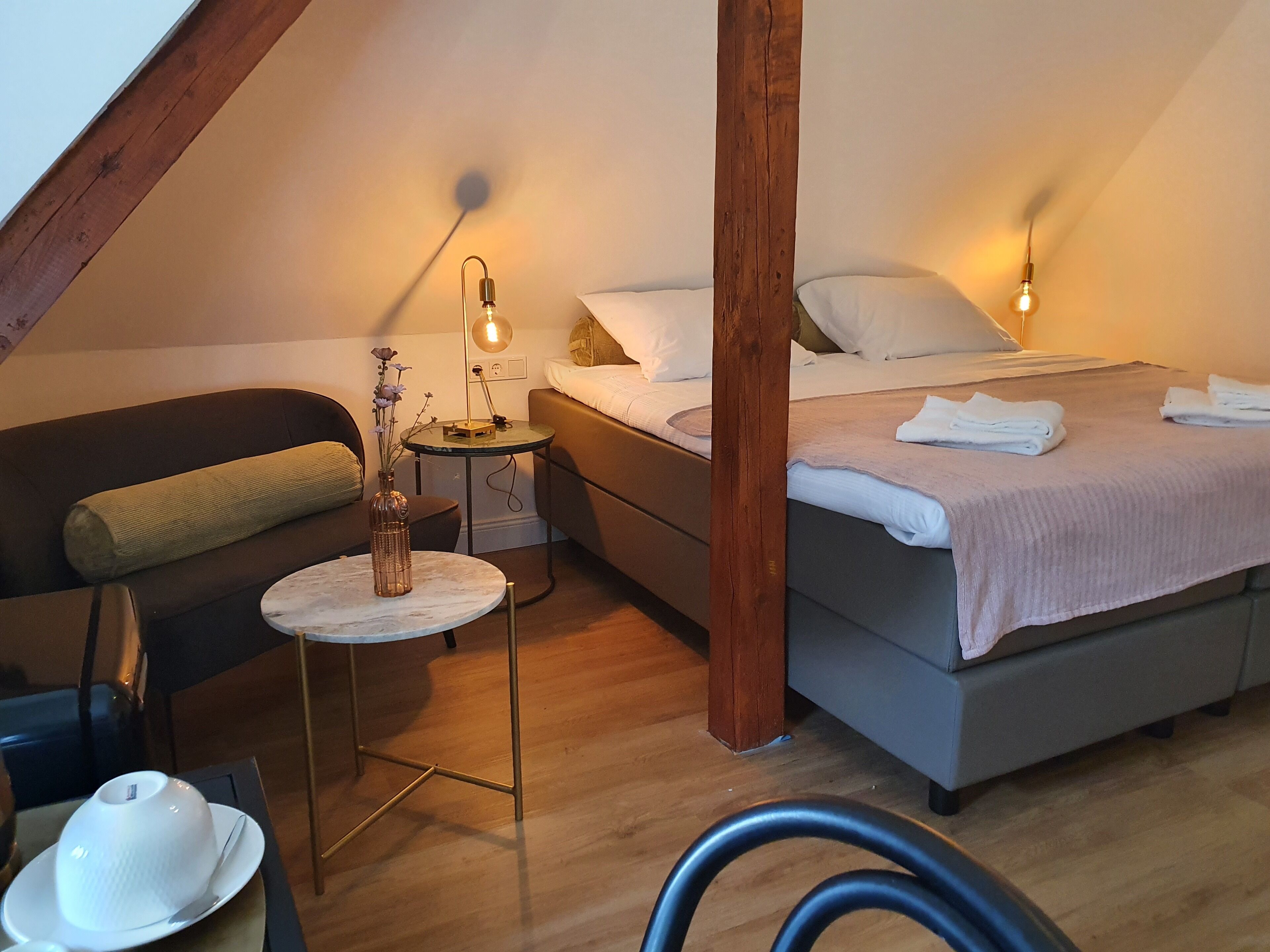 Ein gemütliches Schlafzimmer mit einem Bett, einem kleinen runden Tisch mit einer Vase und einem Sessel.