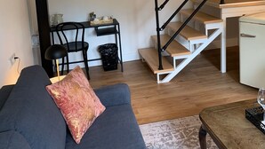 A modern living room with a sofa, a coffee table, a staircase with a railing, a small table with a lamp, and a trash bin. - Boutique Hotel Villa Horbach (Idar-Oberstein)