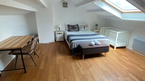 En rummelig stue med en stor seng, et træspisebord og et højtloft med ovenlys.