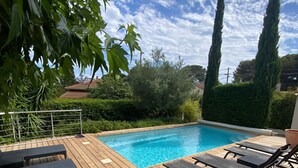 En træterrasse med swimmingpool, omgivet af grønt og høje træer.