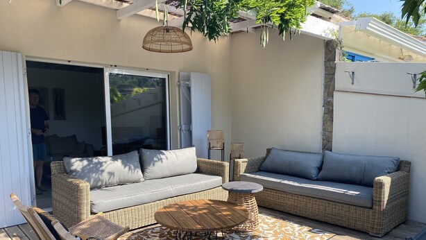En udendørs terrasse med fletmøbler, et rundt bord og en polstret sofa.