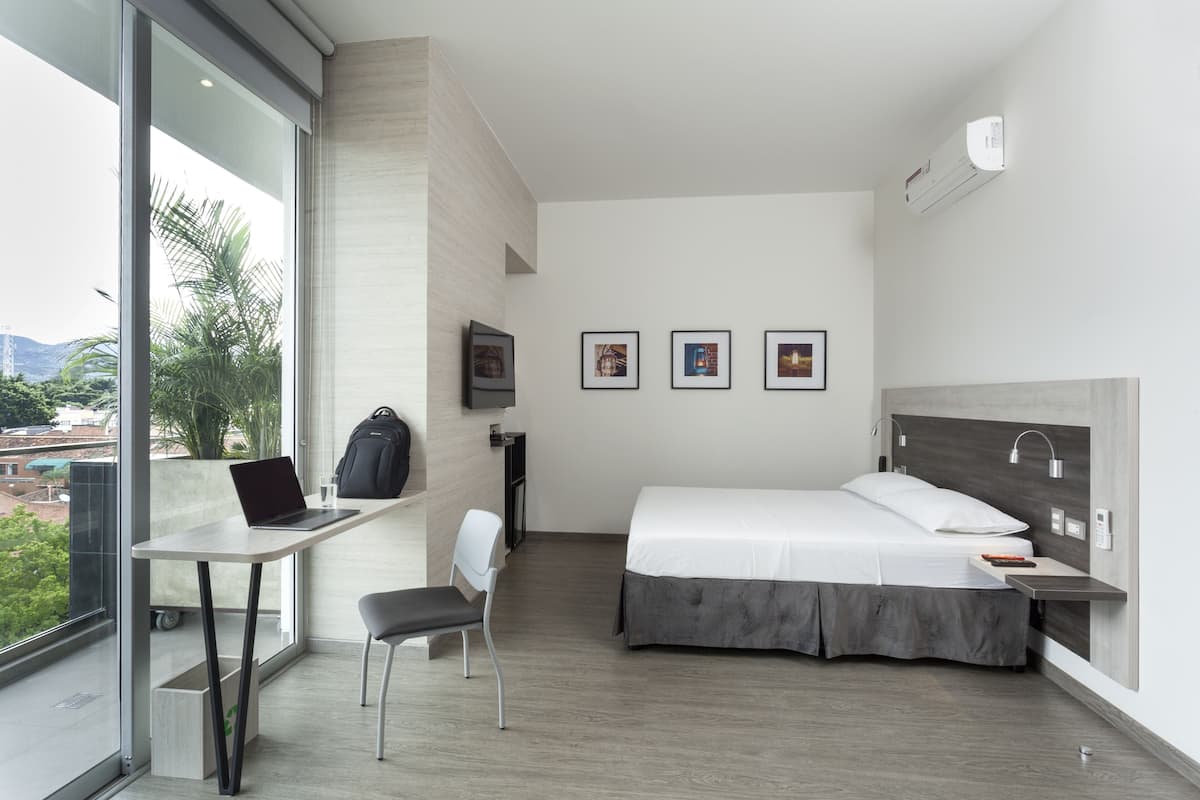 A modern hotel room with a bed, desk, chair, and a large window with a view.