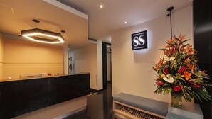 A modern reception area with a black reception desk, a bench, a floral arrangement, and a sign indicating the hotel name. - Hotel Park 85 (Cali)