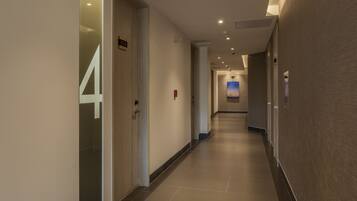 Corredor moderno de hotel com a placa de número '4', iluminação embutida e vista para o hall de entrada ao fundo.