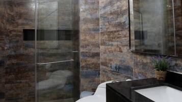 Un baño moderno con ducha de vidrio, inodoro blanco y encimera negra con lavamanos.