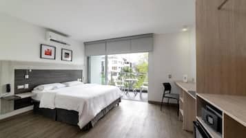 Un dormitorio moderno con una cama grande, un escritorio y un balcón con vistas a edificios.