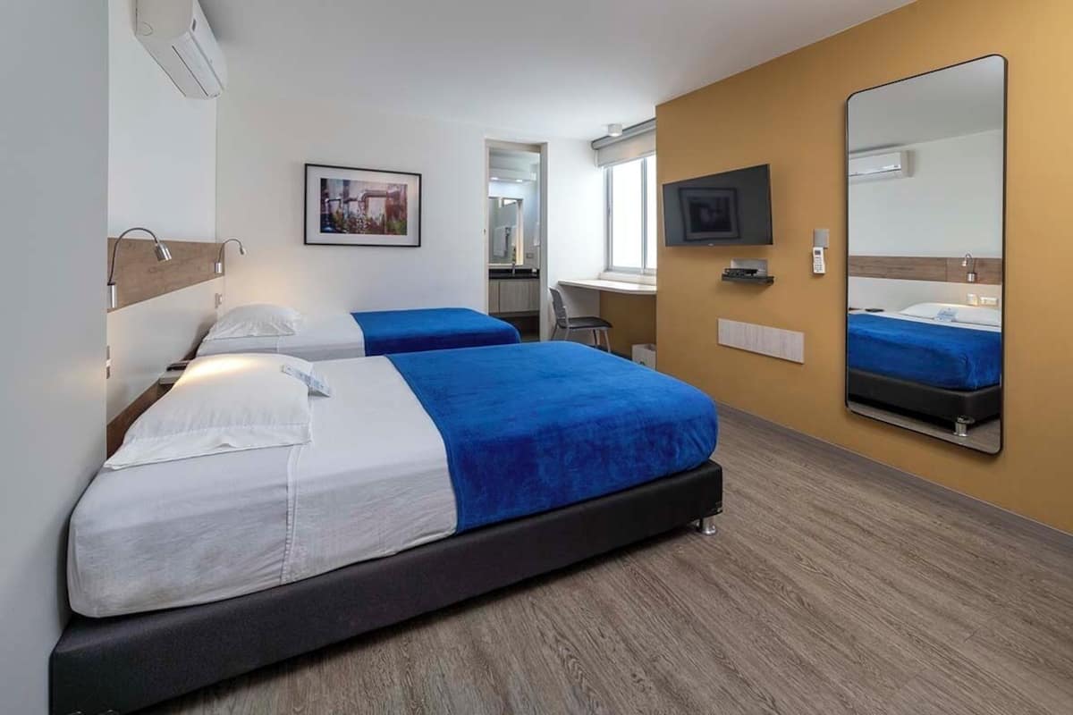 A hotel room with two beds, a TV, a mirror, and a window.