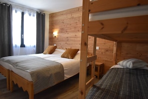 A room with a wooden bunk bed, a single bed, and a small bedside table.