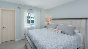 Um quarto com uma cama, mesa de cabeceira, luminária, janela com cortinas e porta.