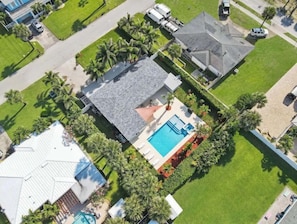 An aerial view of a residential property with a swimming pool, surrounded by well-maintained lawns and palm trees.