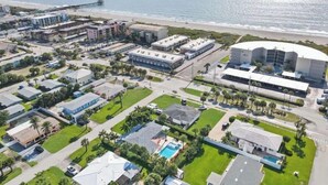 Vista aérea de uma área residencial costeira com um hotel grande, piscina e vista para a praia.