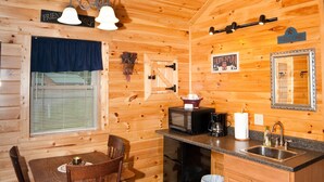 A wooden cabin interior with a dining table, chairs, a kitchen area with a sink, and a microwave.