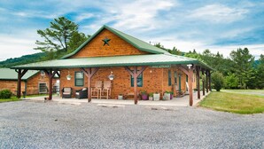 A rustic log cabin with a green roof, a porch with outdoor seating, and a sign indicating an office entrance.