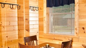 A wooden interior with a dining table, four chairs, a sign reading "Friends & Family Gather Here," and a window with blinds.