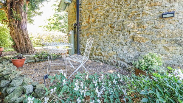 A stone wall, a metal chair, and a table in a garden area. - Old Blacksmiths Cottage (Market Rasen)