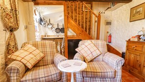 A cozy living room with two plaid armchairs, a small round table, and a wooden staircase. - Old Blacksmiths Cottage (Market Rasen)