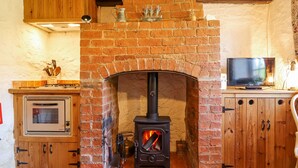 A cozy room with a brick fireplace, a television, and wooden cabinets. - Old Blacksmiths Cottage (Market Rasen)