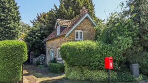 A stone house with a tiled roof, surrounded by well-maintained hedges and trees. - Old Blacksmiths Cottage (Market Rasen)