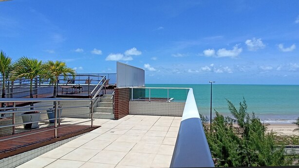 Terraza en la azotea con vistas al océano, que cuenta con una piscina, zona de estar y palmeras.