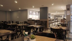 Un comedor moderno con varias mesas y sillas, una cocina al fondo y cuadros en la pared.