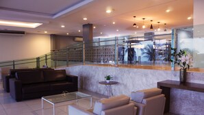 Un vestíbulo moderno con una mesa de centro de vidrio, sofás, un mostrador de recepción y una escalera con barandales de cristal.