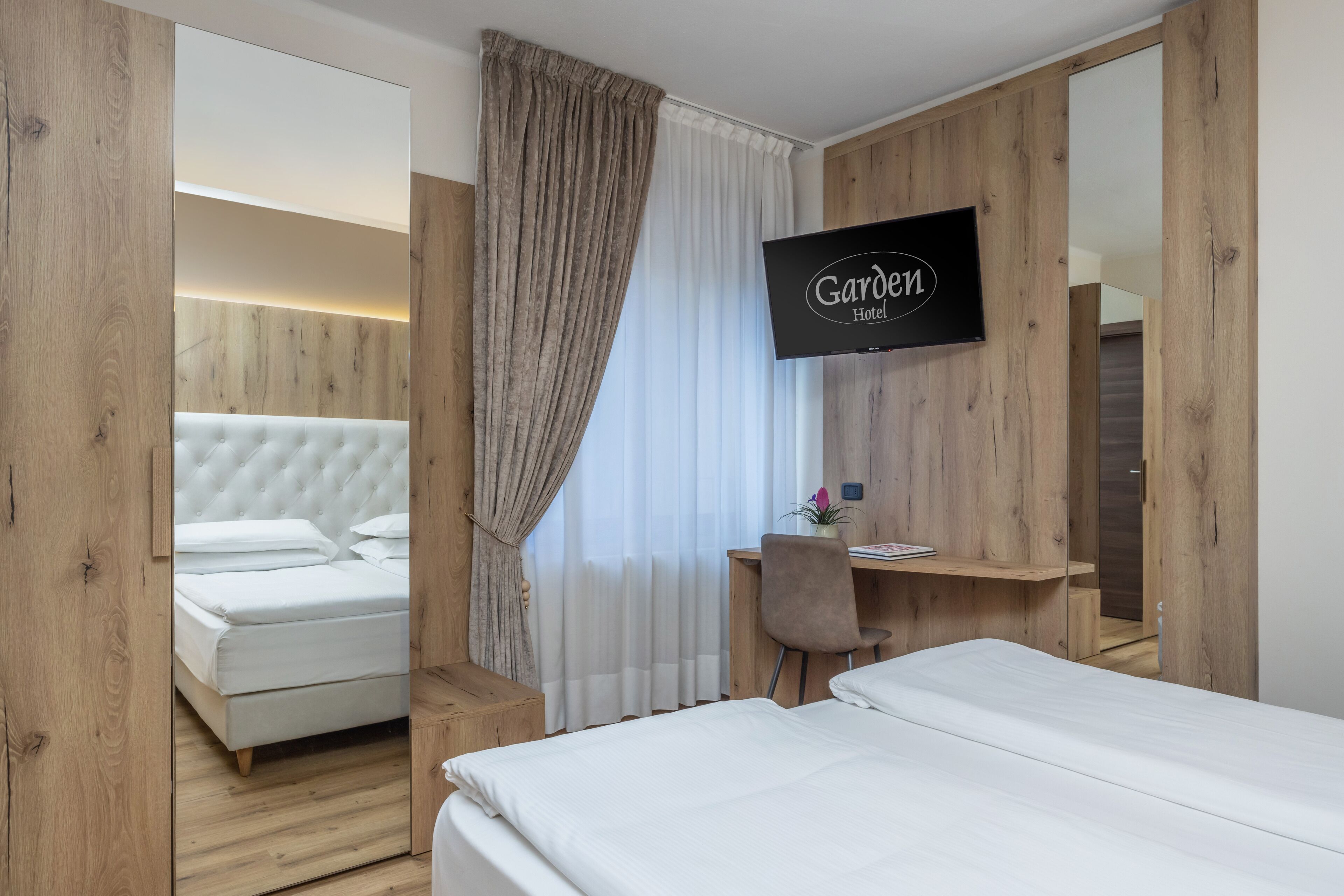 A hotel room with a bed, a desk, a chair, a TV, and a mirror.