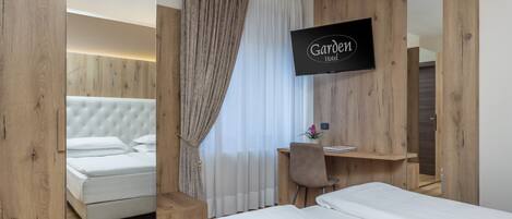 A hotel room with a bed, a desk, a chair, a TV, and a mirror.