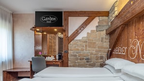 A hotel room with a stone wall, a bed, a desk with a chair, a coffee maker, and a sign that reads "Garden Hotel". - Hotel Garden (Andalo)