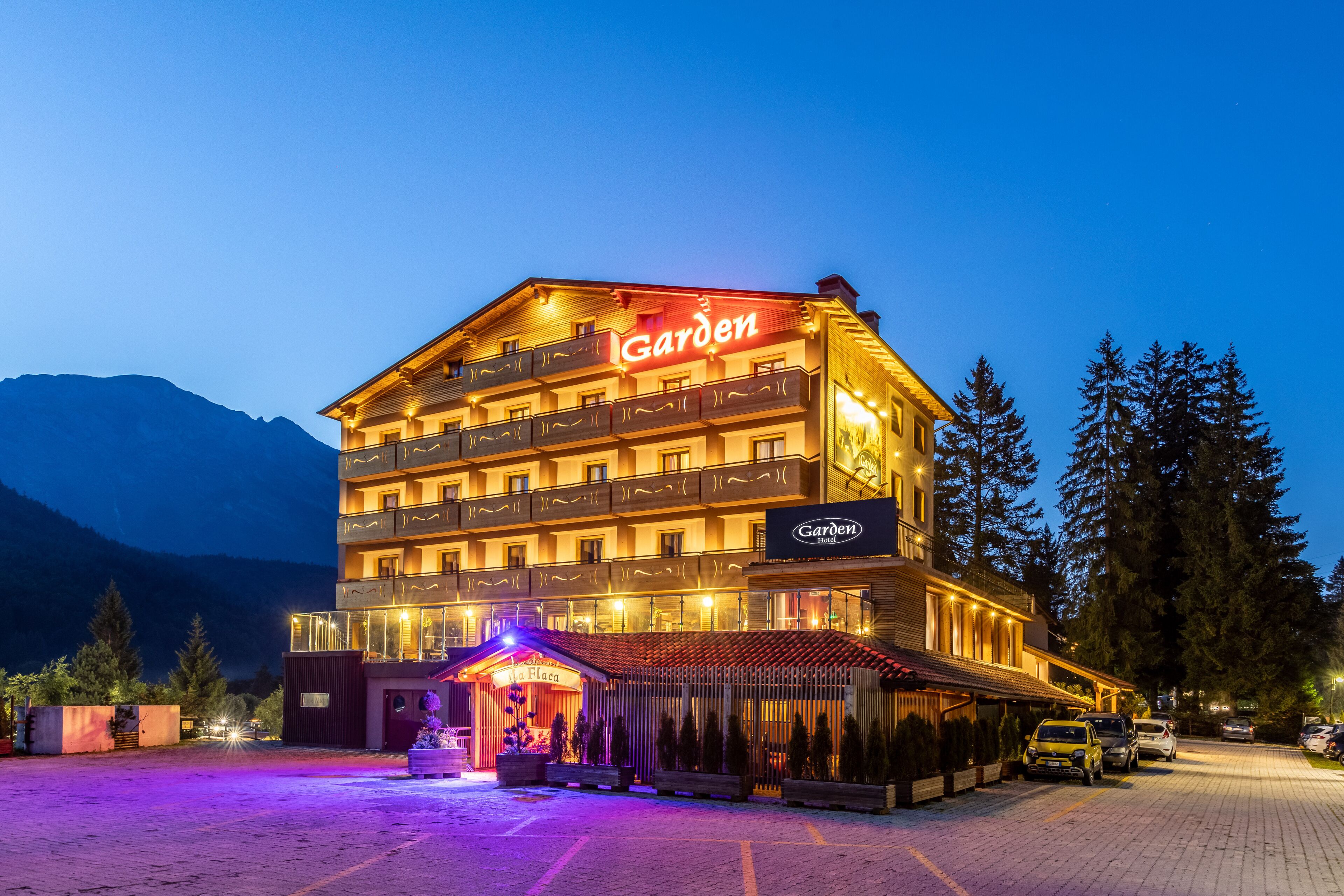 Un hotel a più piani con un cartello ben visibile con la scritta 'Garden', una zona esterna coperta e un parcheggio.