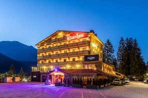 Un hotel de varios pisos con un letrero llamativo que dice 'Garden', un área al aire libre techada y un estacionamiento.