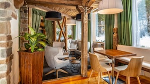 A cozy interior with a wooden ceiling, a dining area with a wooden table and chairs, and a seating area with armchairs and a sofa. - Hotel Garden (Andalo)